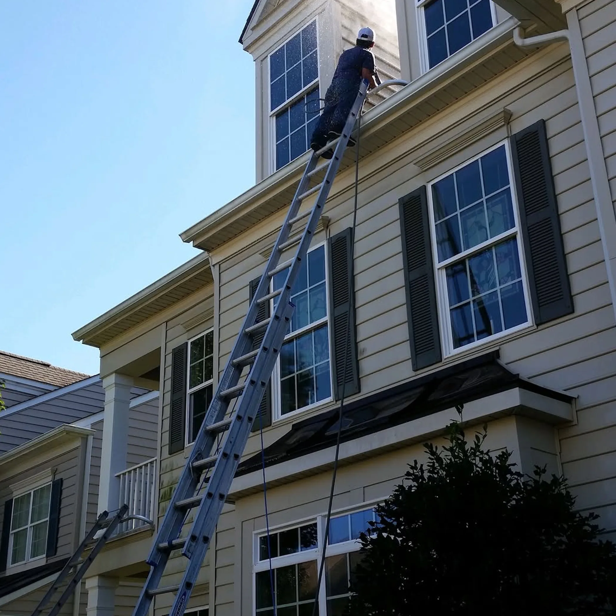 person pressure washing house exterior ladder